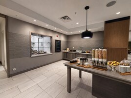 Una cafetería moderna con mostrador, zona de estar y diversas opciones de comida y bebida.