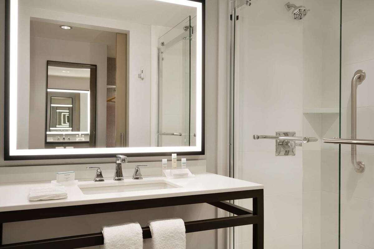 A modern bathroom with a large mirror, a white sink, and a glass shower enclosure.