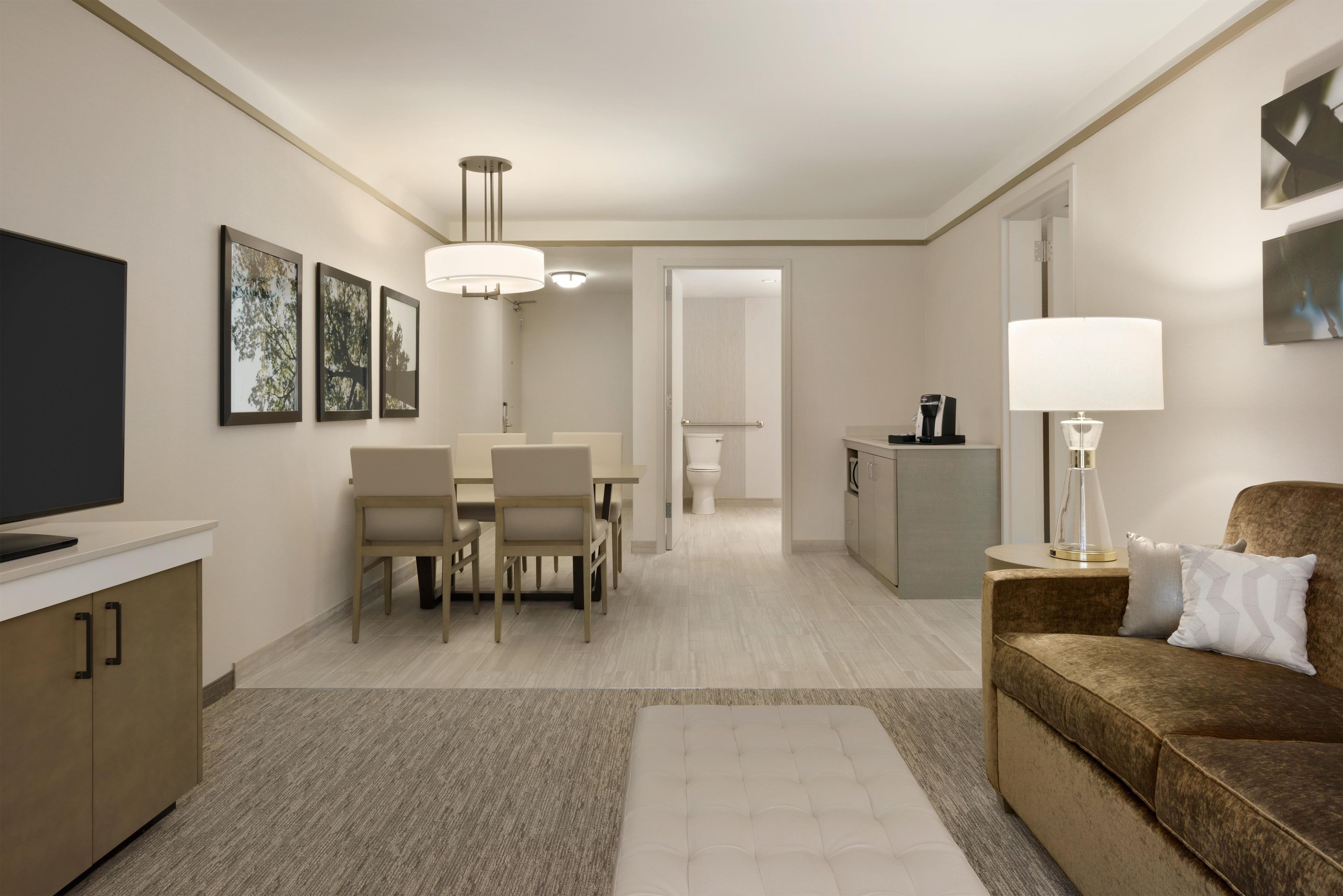 A modern hotel room with a dining area, a sofa, a TV, and a coffee machine.