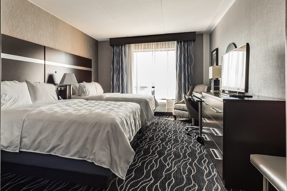 A hotel room with two beds, a desk, a chair, a television, and a large window with curtains.