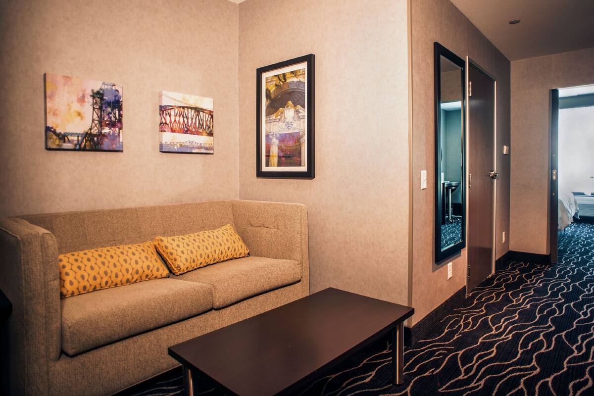 A hotel room with a sofa, a coffee table, and three framed artworks on the wall.