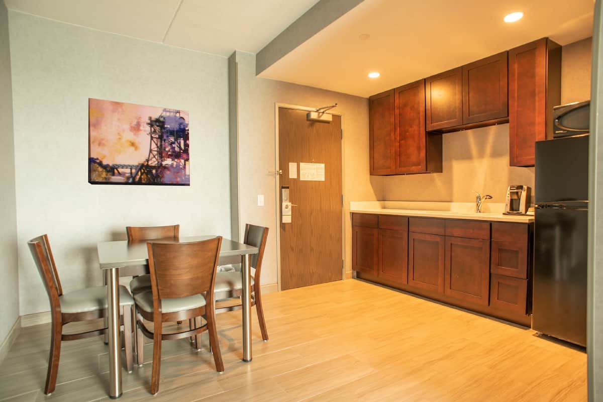 A modern kitchen with wooden cabinets, a stainless steel refrigerator, and a dining area with a table and chairs.