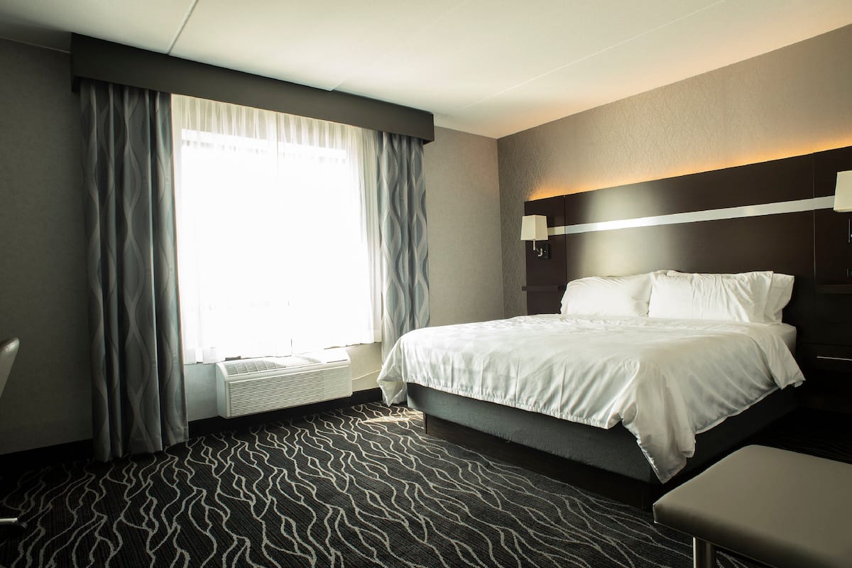 A hotel room with a large bed, a bedside table, a lamp, and a window with curtains.