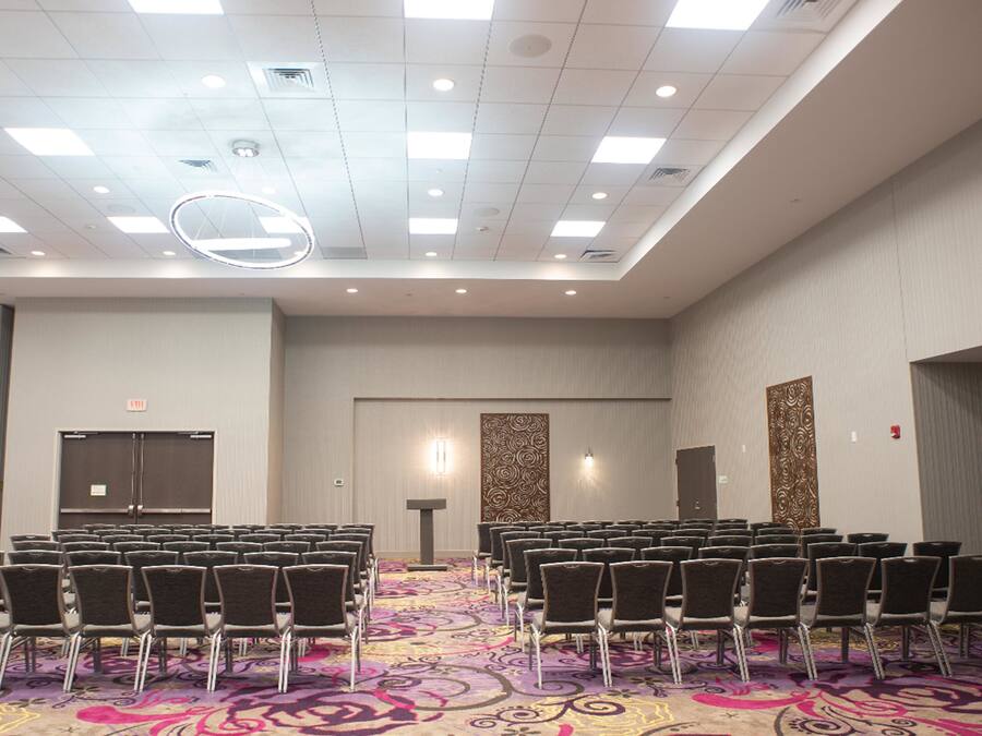 A conference room with rows of chairs, a patterned carpet, and a ceiling with recessed lighting and a circular light fixture.