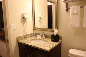 Un baño con lavamanos de granito, un secador de pelo, un perchero para toallas y un inodoro.