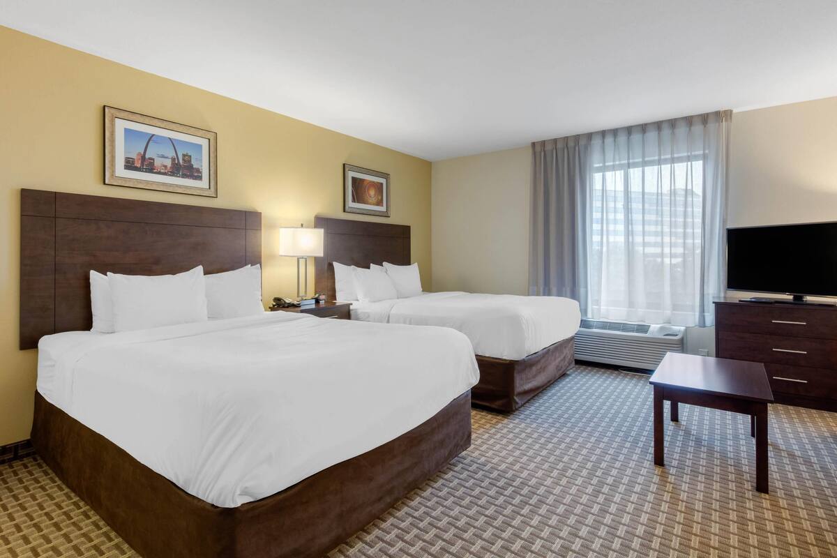Ein Hotelzimmer mit zwei Betten, einem Fernseher, einem Schreibtisch und einem großen Fenster mit Vorhängen.