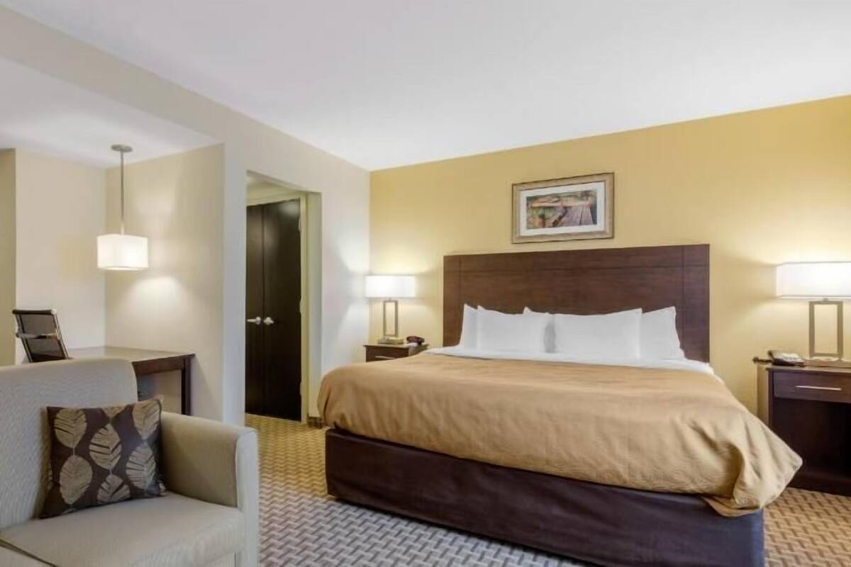 Ein Hotelzimmer mit einem Bett, einer Couch, zwei Nachttischen mit Lampen, einer Tür und einem gerahmten Bild an der Wand.