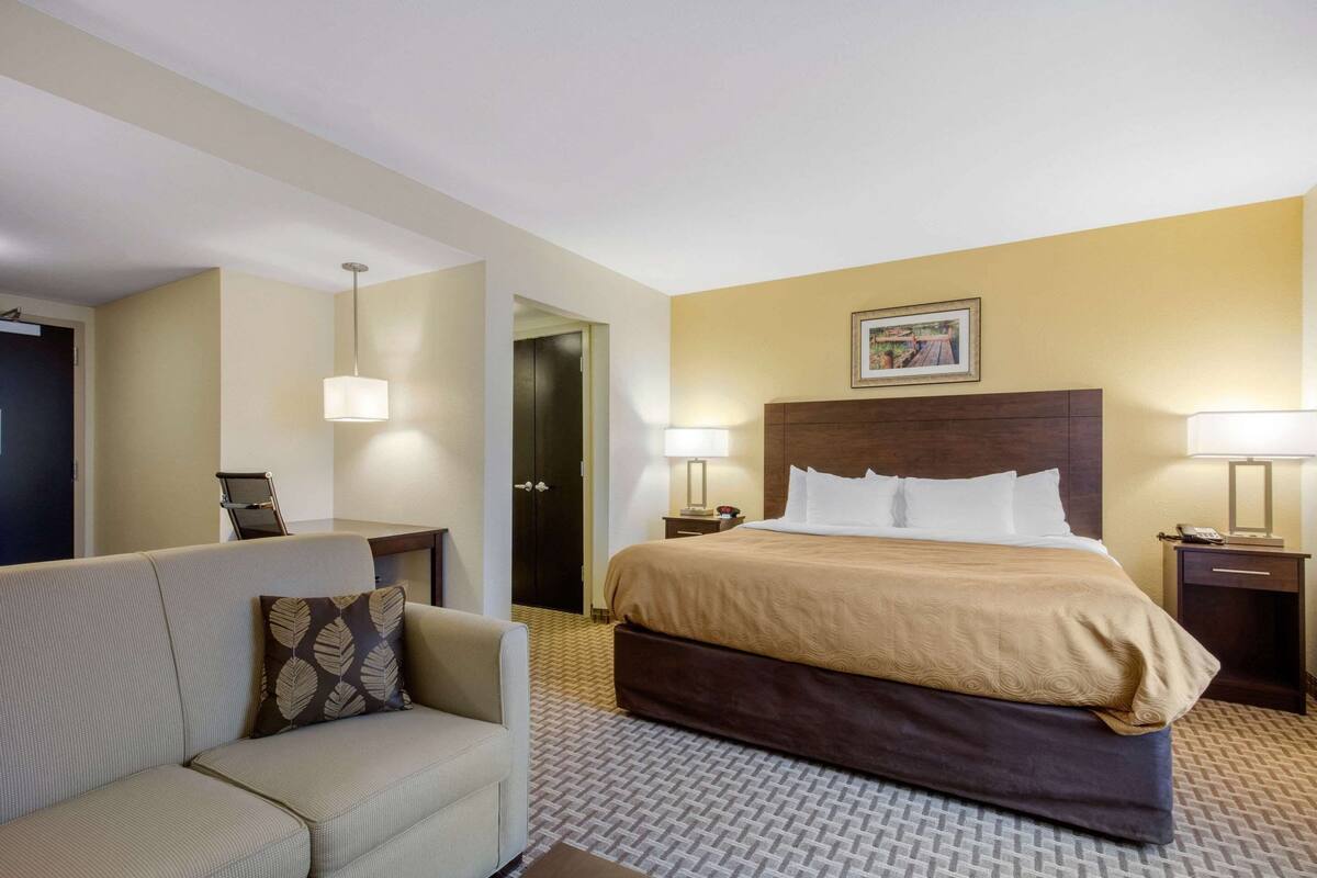 Ein Hotelzimmer mit Bett, Sofa, zwei Nachttischlampen, einem Nachttisch und einer Tür zu einem Badezimmer.