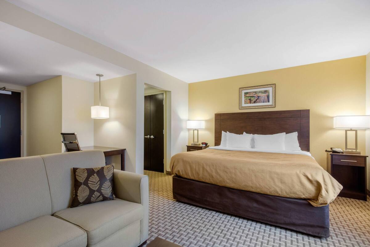Ein Hotelzimmer mit einem großen Bett, einer Couch, einem Schreibtisch und einer Tür zum Badezimmer.