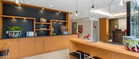 Eine moderne Küche mit Holzausstattung, einer schwarzen Arbeitsplatte und einer Obstschale. Drei Pendelleuchten und ein Kühlschrank sind im Hintergrund zu sehen.