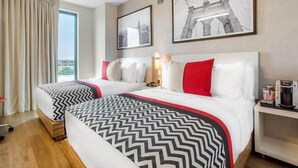 Habitación de hotel con dos camas, un ventanal con cortinas, una cafetera y cuadros en la pared.