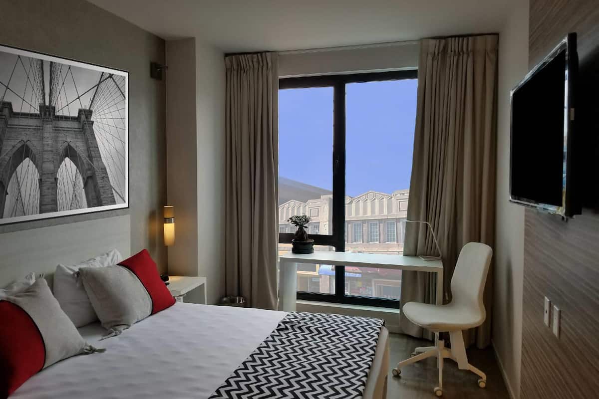 A hotel room with a large bed, a desk with a chair, a TV, and a window with curtains.