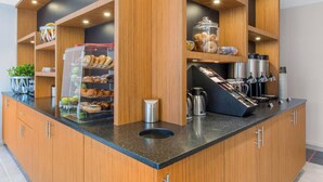 Una barra de desayuno con armarios de madera, un espacio para café y una variedad de pasteles y productos de panadería exhibidos en recipientes transparentes.