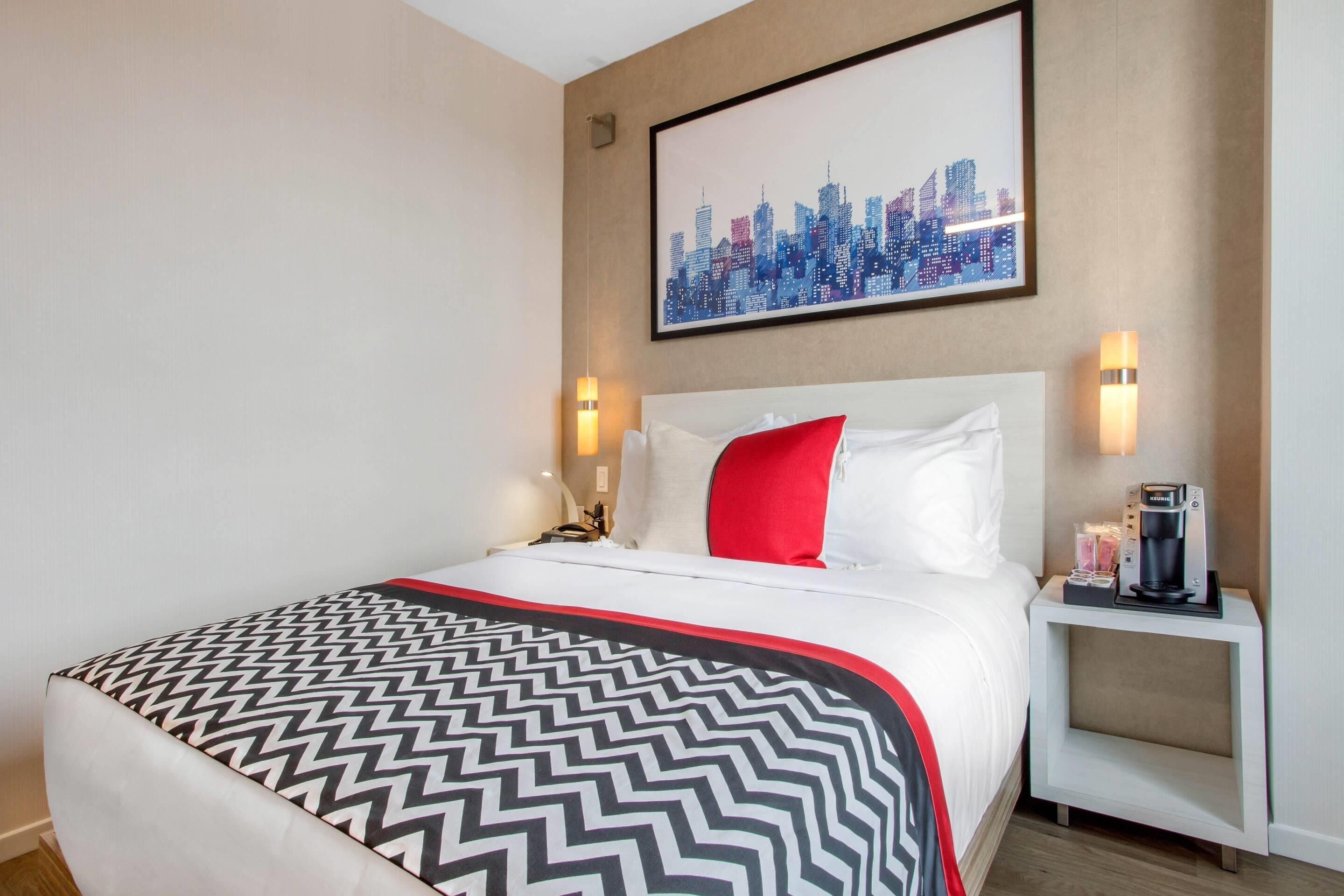Een hotelkamer met een bed, een nachtkastje met koffiezetapparaat en een stadsgezichtschilderij aan de muur.