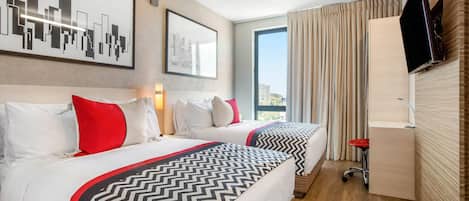 Habitación de hotel con dos camas, televisión, escritorio y un amplio ventanal con cortinas.