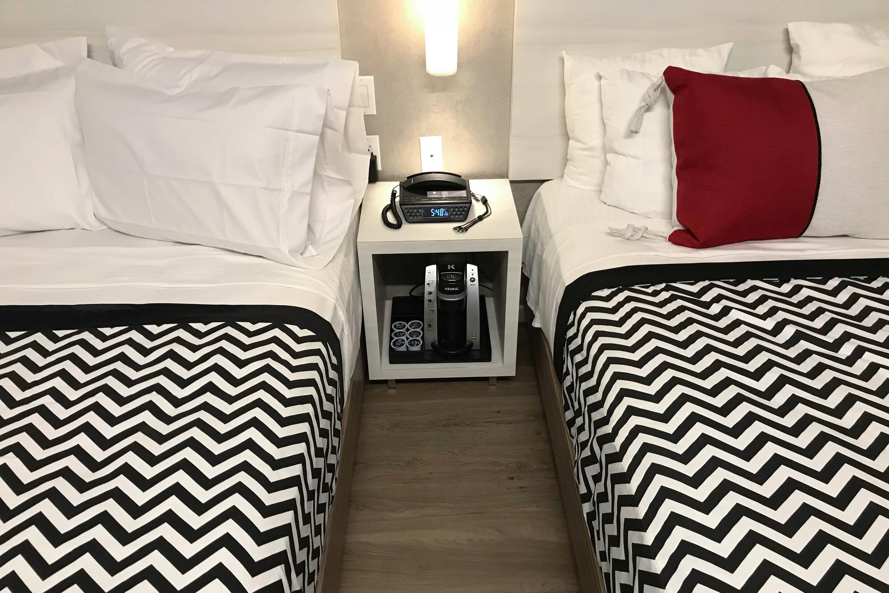 Une chambre d’hôtel avec deux lits, une table de chevet avec une machine à café et un téléphone fixé au mur.