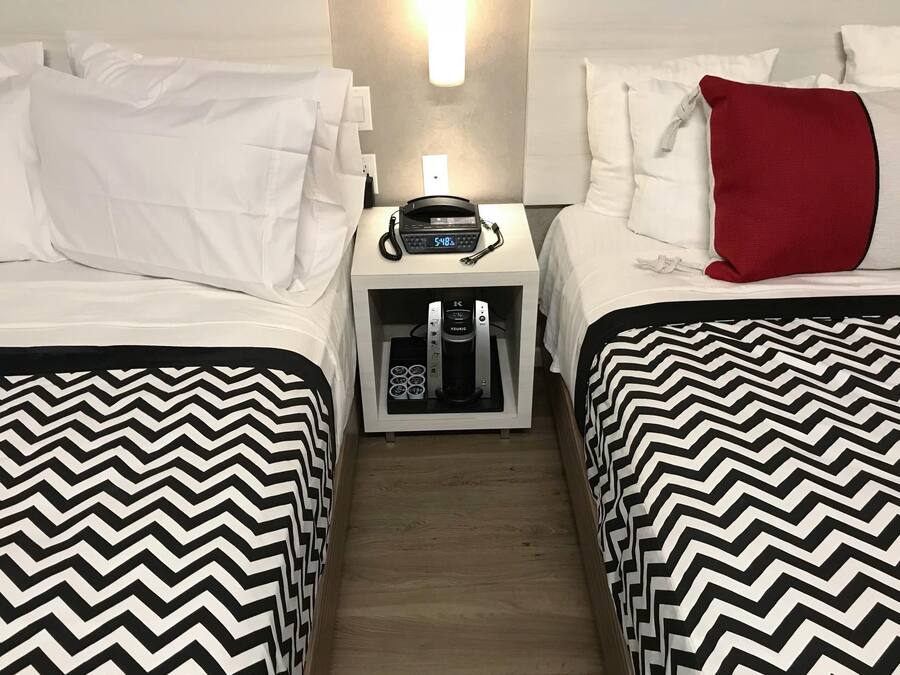 Een hotelkamer met twee bedden, een nachtkastje met koffiezetapparaat en een aan de muur bevestigde telefoon.