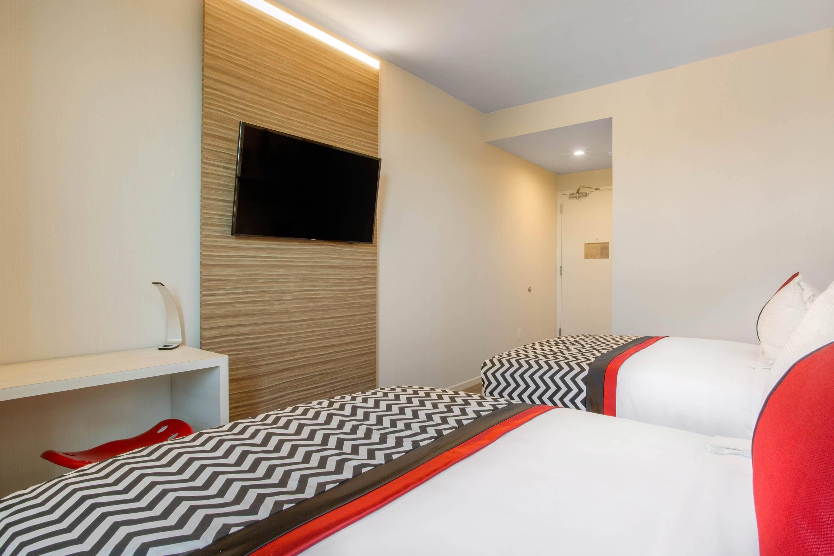 Una camera d'albergo con due letti, una TV a parete, una scrivania e una sedia rossa.
