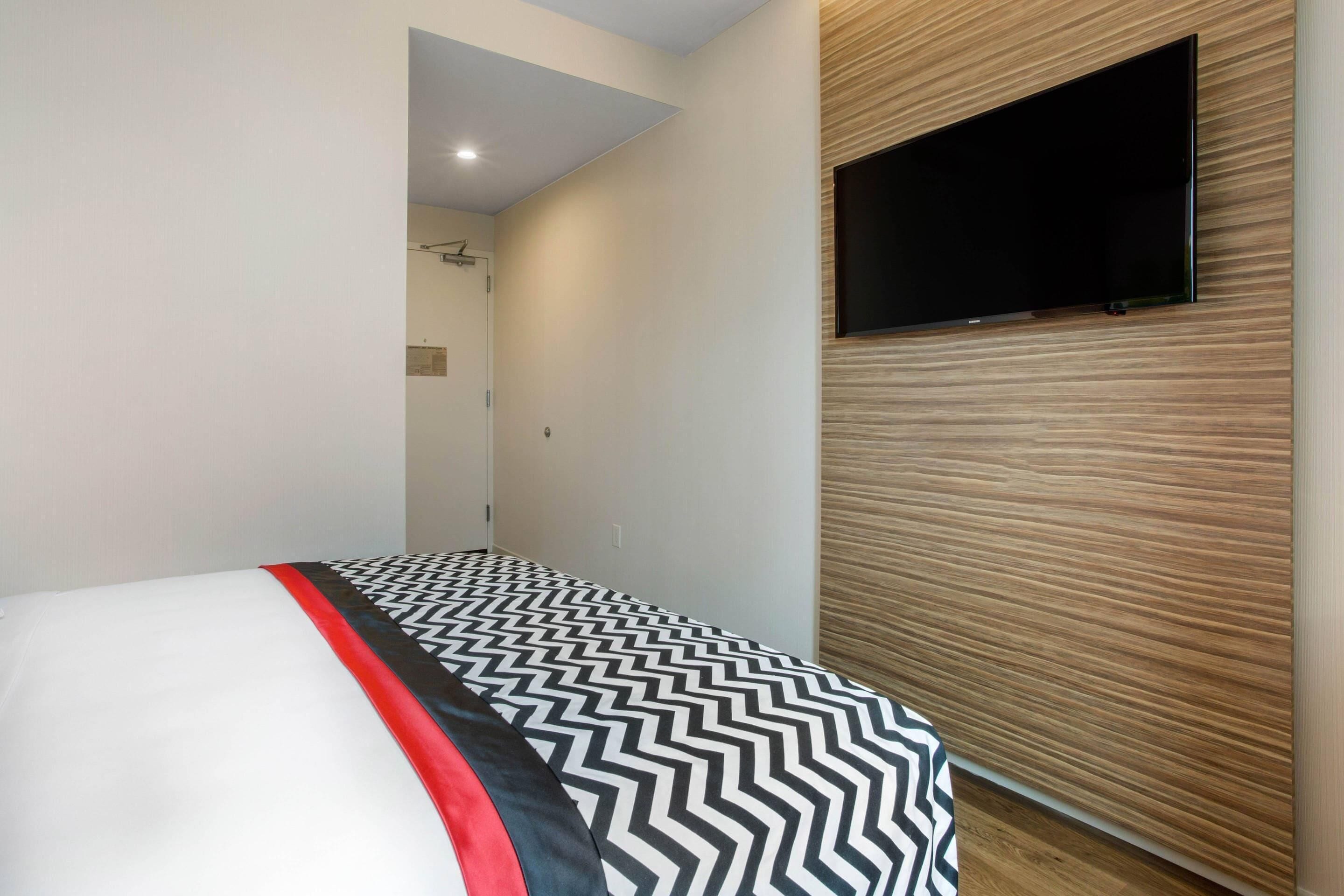 Habitación de hotel con cama, televisión montada en la pared y diseño de paneles de madera.