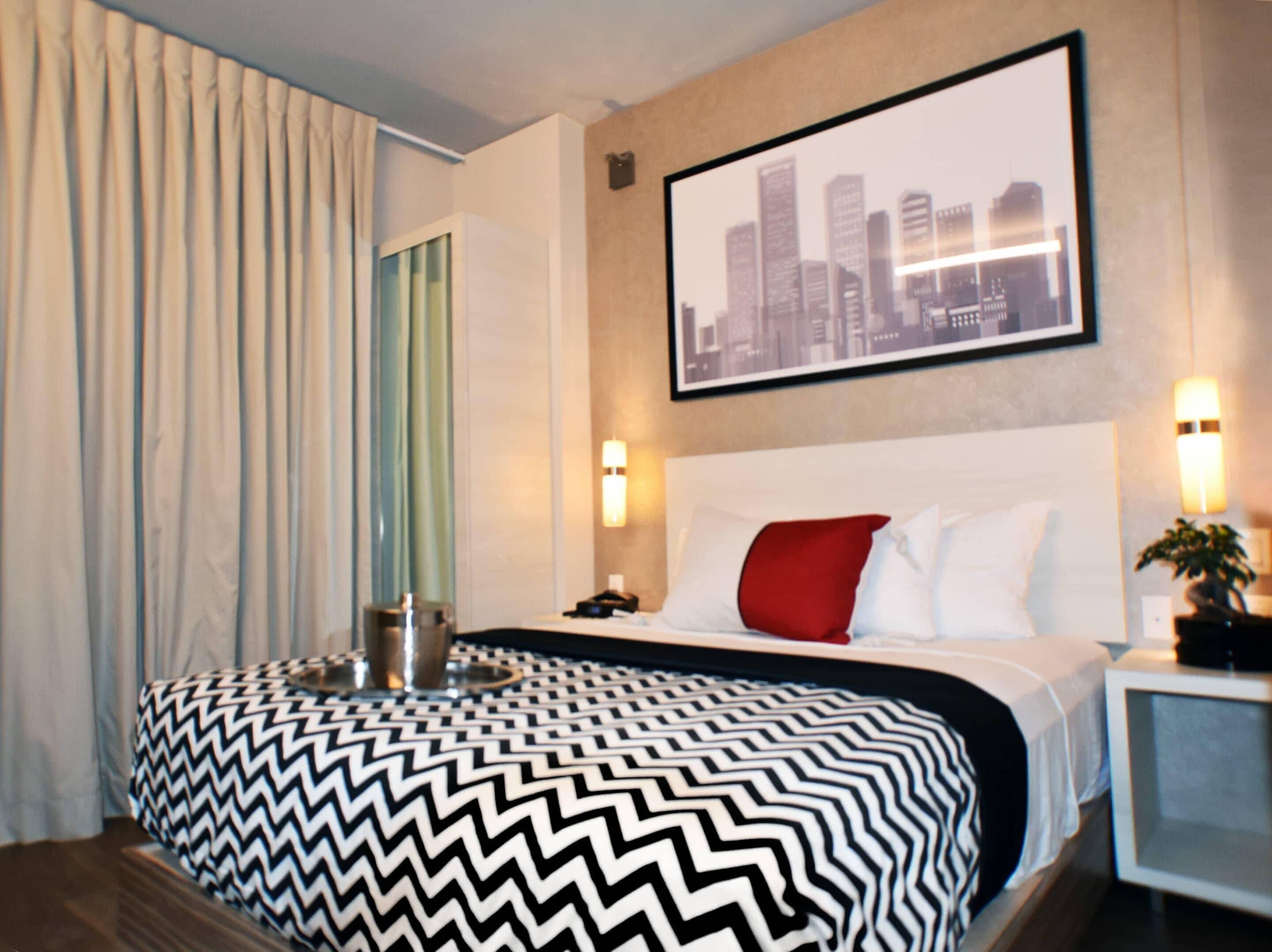 A hotel room with a bed, a cityscape painting, a nightstand, and a lamp.