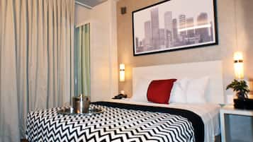 A hotel room with a bed, a cityscape painting, a nightstand, and a lamp.