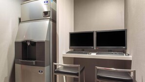 Una kitchenette compacta con refrigerador, dos monitores, un teclado y dos sillas.