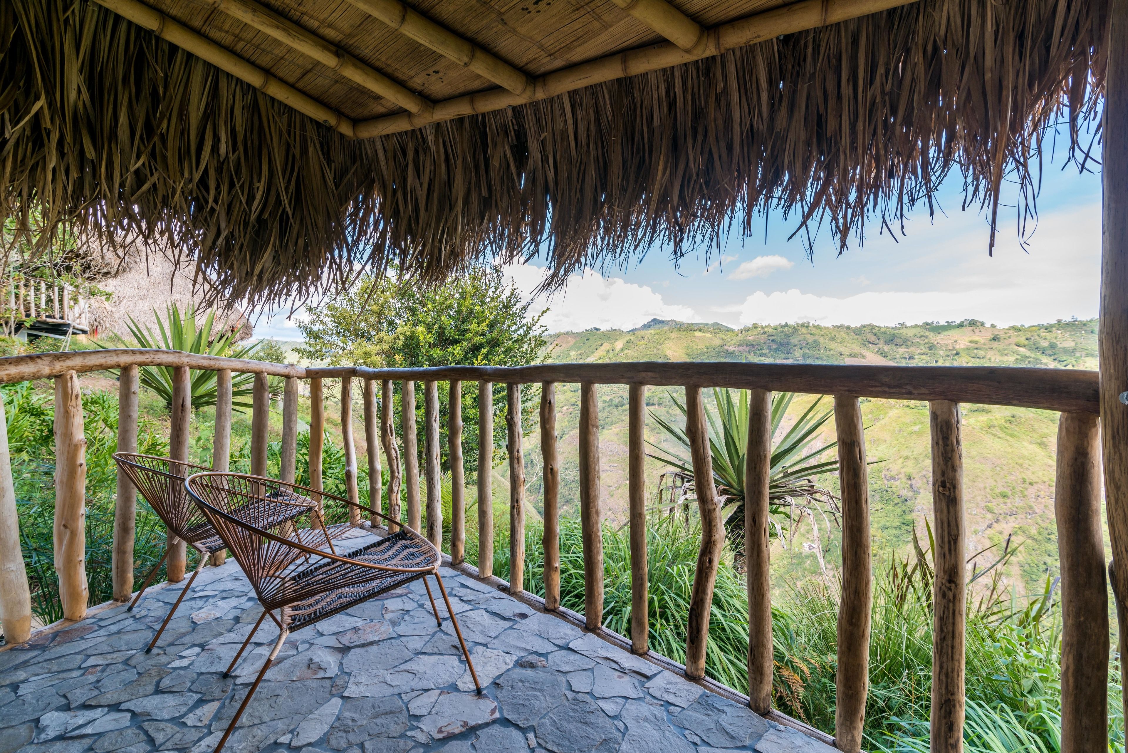 A covered outdoor seating area with a stone floor and a view of a hilly landscape.