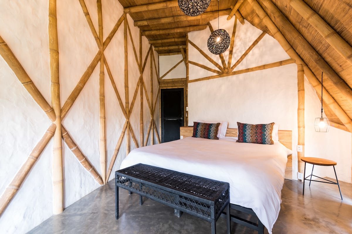 A bedroom with a large bed, a bench, and a hanging light fixture.