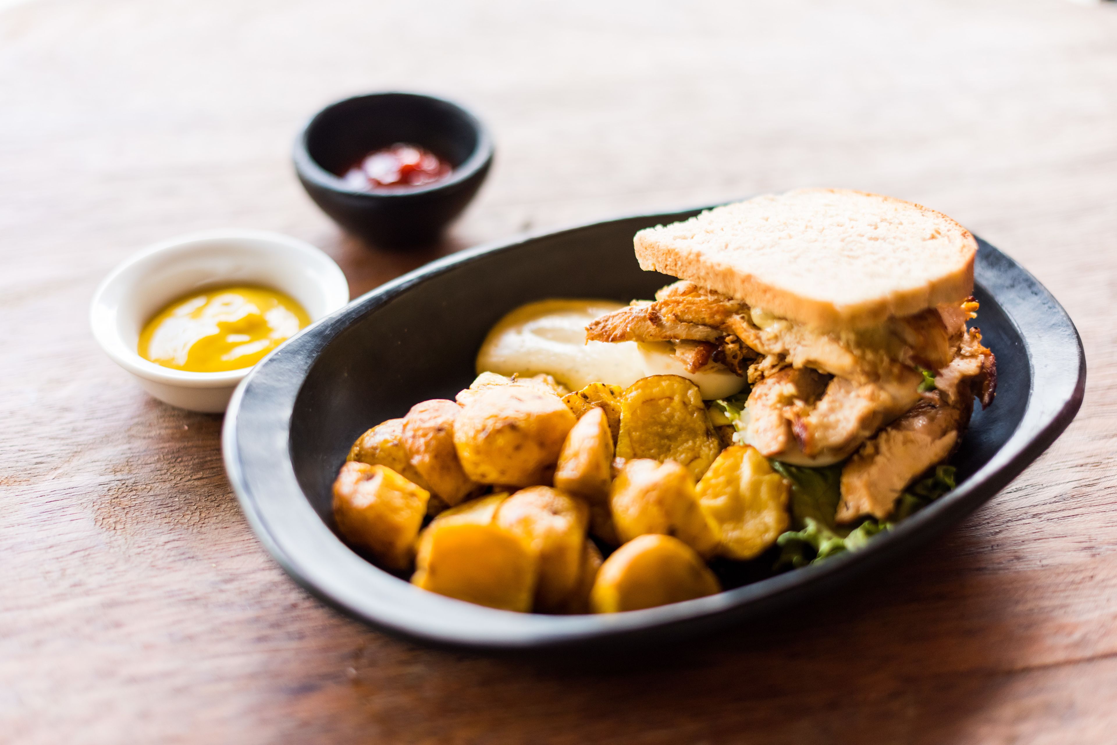 Une assiette avec un sandwich, des frites en forme de quartiers de pommes de terre et deux petits ramequins de condiments.