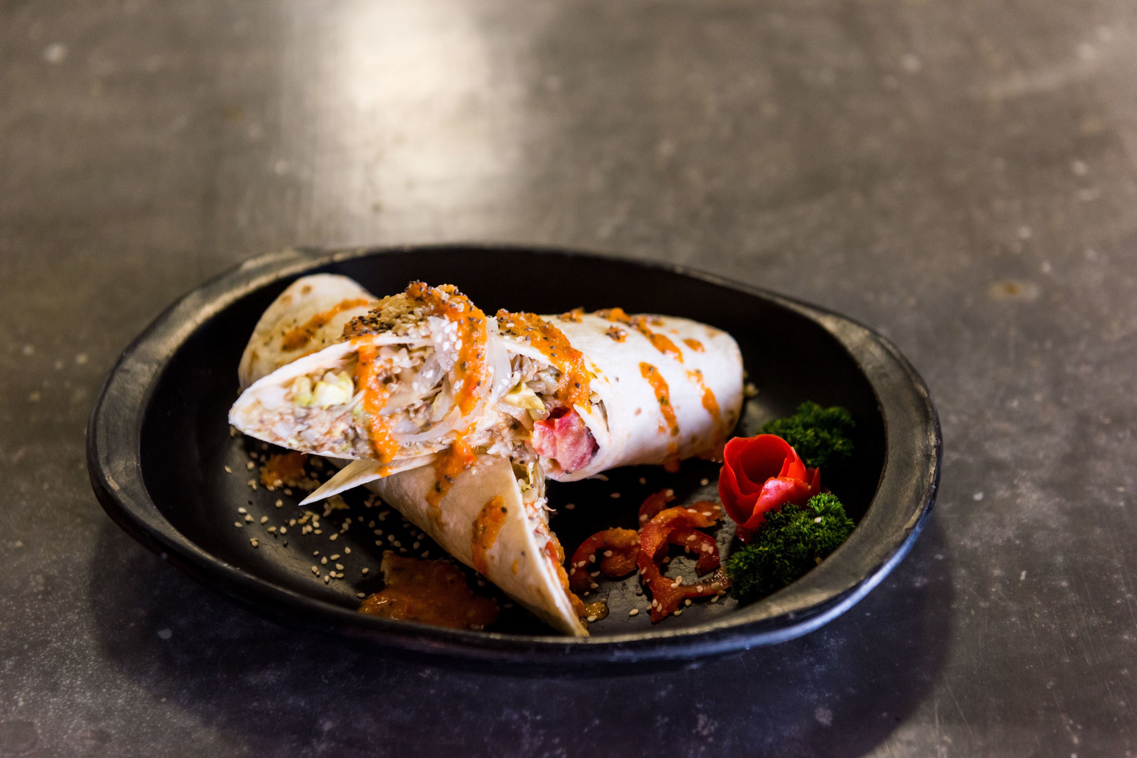 A seafood dish on a black plate with sesame seeds and a red garnish.