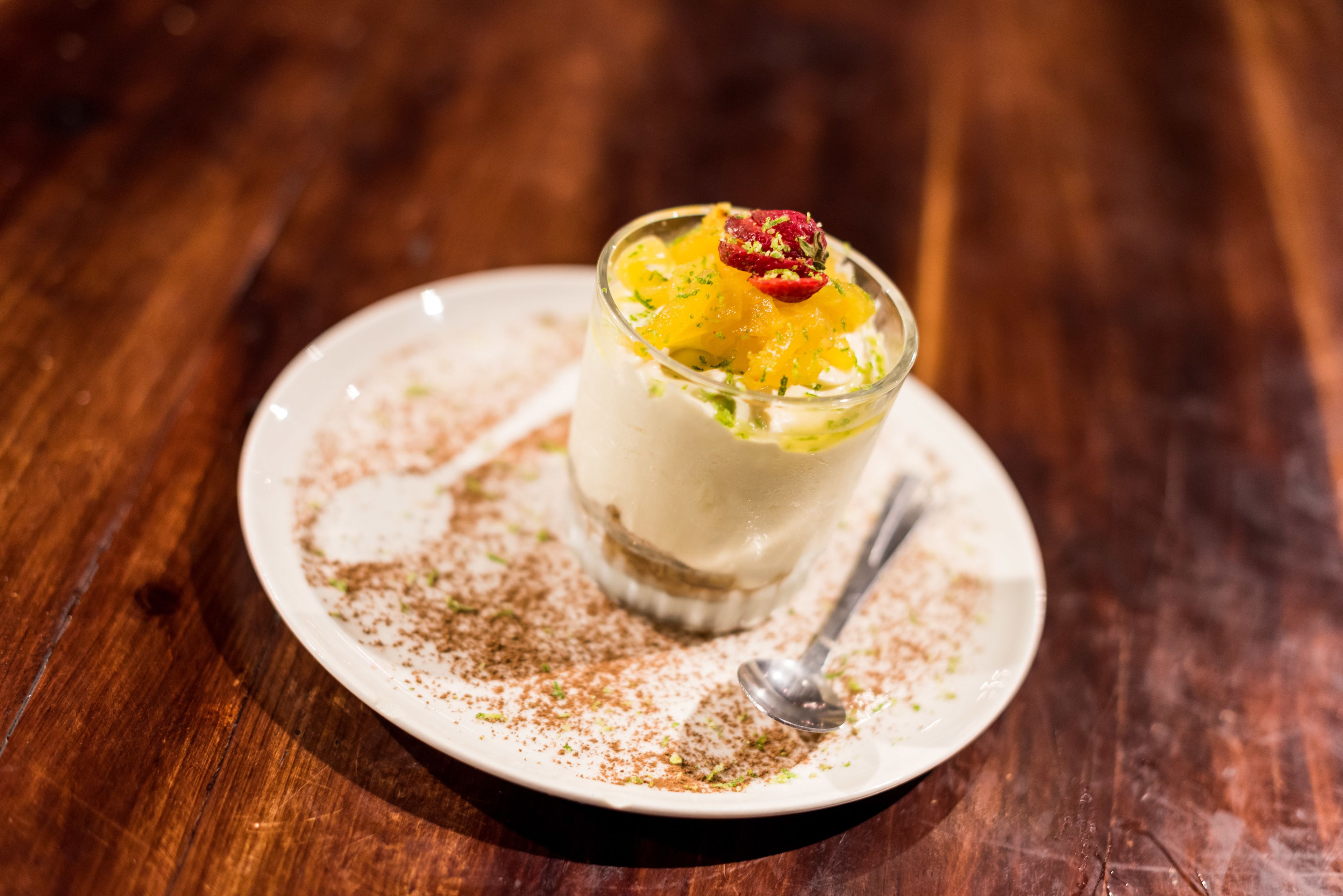 Postre en un plato blanco con una cuchara, sobre una mesa de madera.