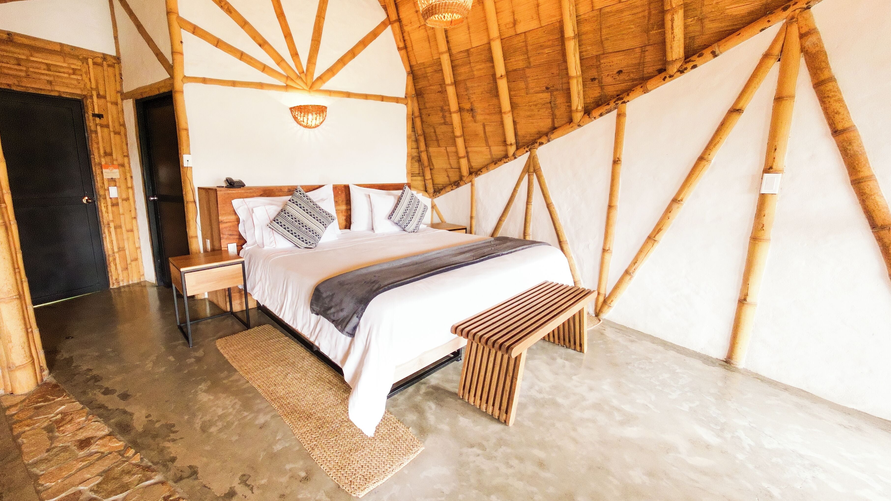 A room with a bed, a nightstand, a woven rug, and a bench.