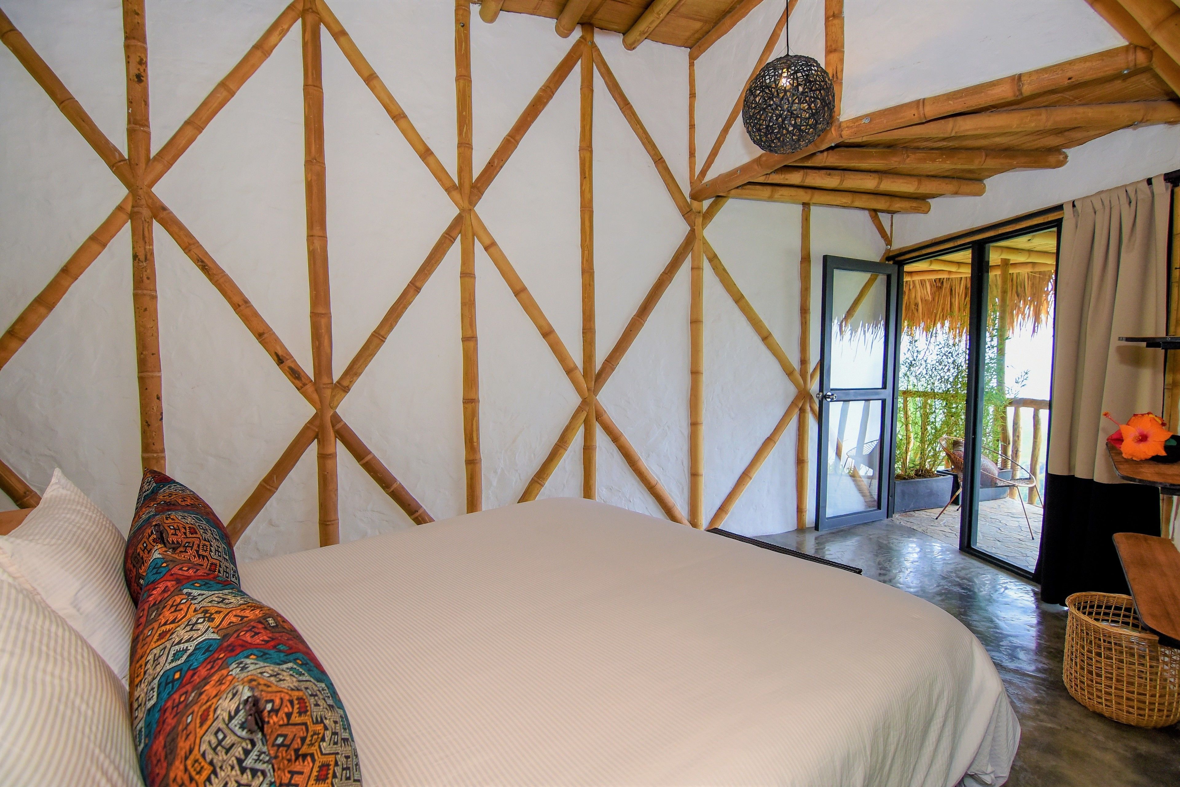 Une chambre dotée d’un grand lit, d’une structure de plafond en bois et offrant une vue sur l’extérieur grâce à une porte vitrée.