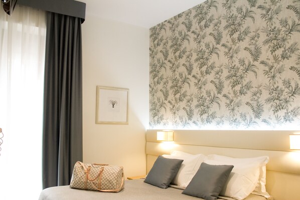 Une chambre d’hôtel avec un lit, une table de chevet, une lampe, un tableau encadré et un papier peint à motifs floraux.