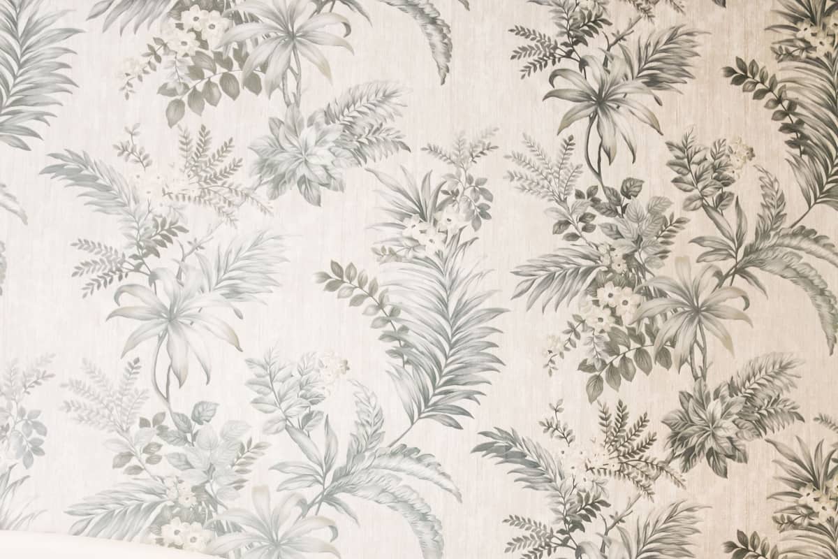 Une pièce avec un papier peint à motifs floraux, un canapé gris et un coussin gris.