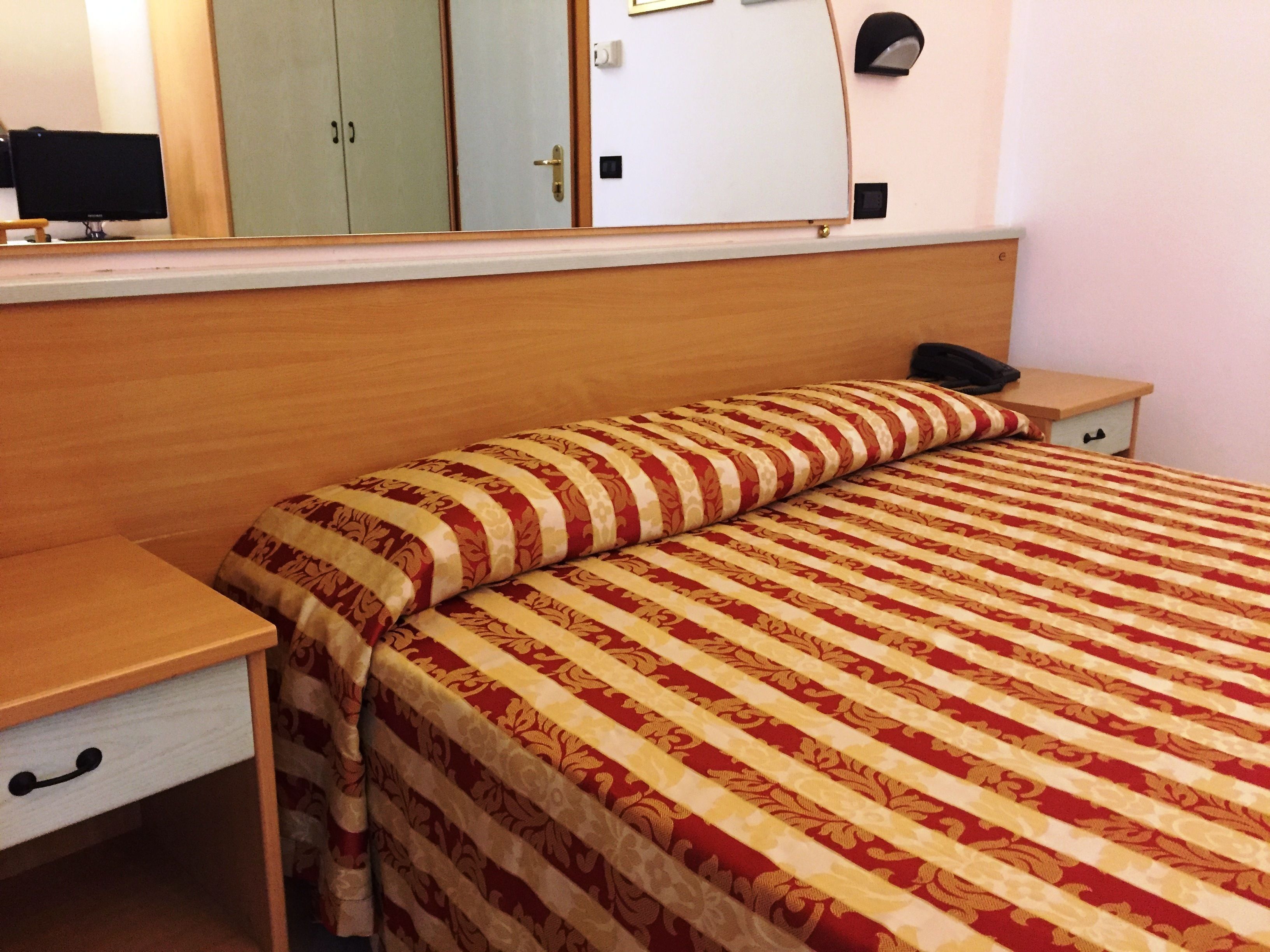 Quarto de hotel com uma cama, mesa de cabeceira, escrivaninha e guarda-roupa.