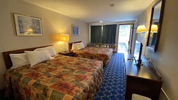 Une chambre d’hôtel avec deux lits, un bureau, une chaise, une poubelle et une grande fenêtre avec des rideaux.