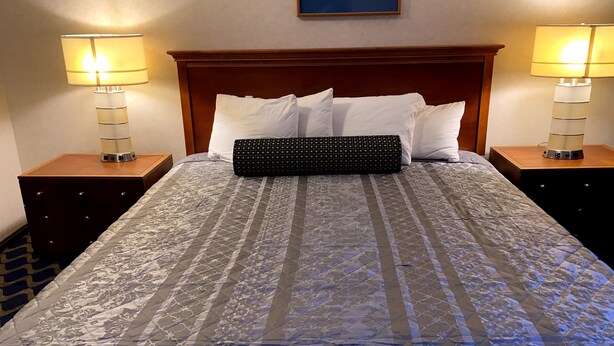 A neatly made bed with a patterned bedspread, two bedside lamps, and a framed picture on the wall. - Economy Lodge (Fiskdale)