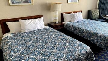 Une chambre d’hôtel avec deux lits, chacun recouvert d’une couvre-lit à motifs, une table de chevet avec une lampe et des œuvres d’art encadrées accrochées aux murs.