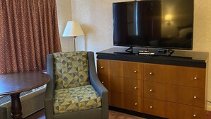 A hotel room with a television, a patterned armchair, a wooden cabinet, and a table. - Economy Lodge (Fiskdale)