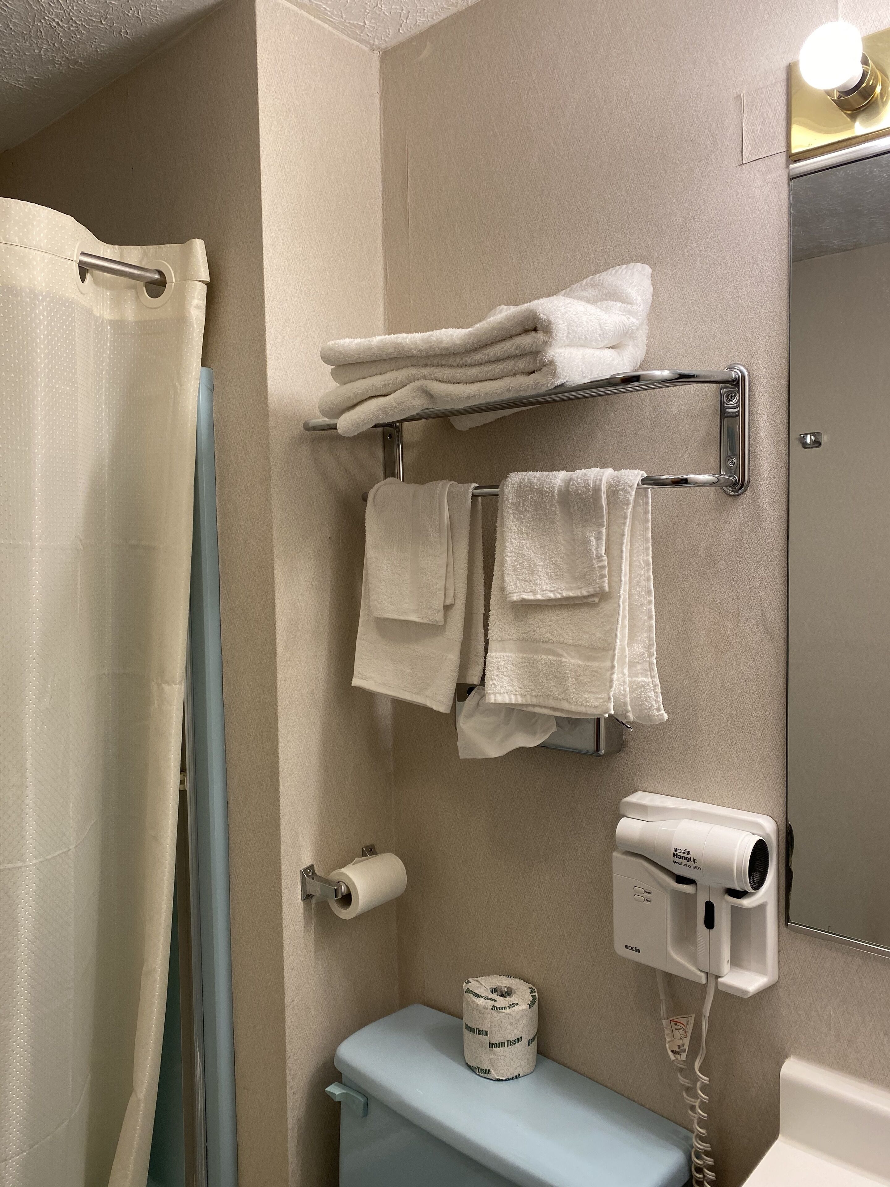 A bathroom with a toilet, a towel rack with folded towels, a toilet paper holder, and a hairdryer.