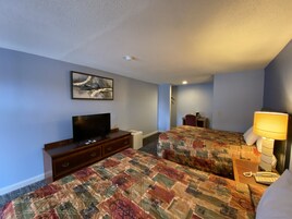 Habitación de hotel con dos camas, televisión, escritorio, lámpara y un cuadro en la pared.
