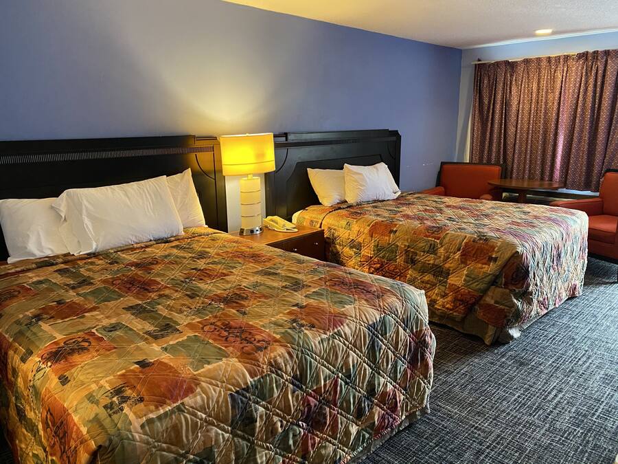 A hotel room with two beds, a nightstand with a lamp, a telephone, and a small table.