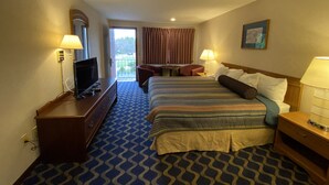 A hotel room with a bed, a desk, a television, and a balcony with curtains. - Economy Lodge (Fiskdale)