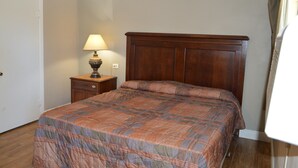 A bedroom with a wooden bed, a nightstand with a lamp, and a door. - Paradise Inn (Bay City)