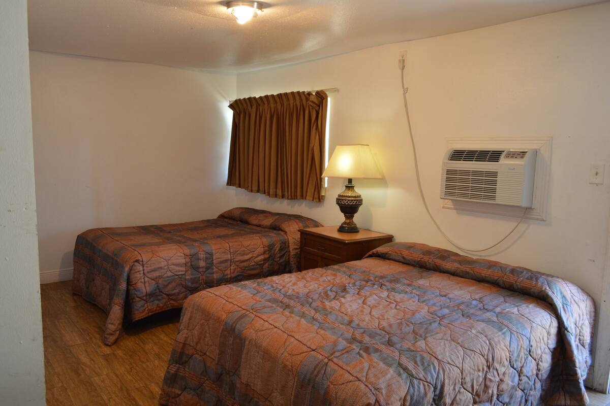 Une chambre avec deux lits, une lampe, un climatiseur et une fenêtre avec des rideaux.