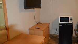 A small room with a television mounted on the wall, a microwave on a small cabinet, and a wooden dresser with a remote control on top. - Paradise Inn (Bay City)