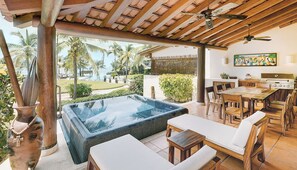 Área de piscina com hidromassagem, mobiliário de madeira e vista para palmeiras e o oceano.