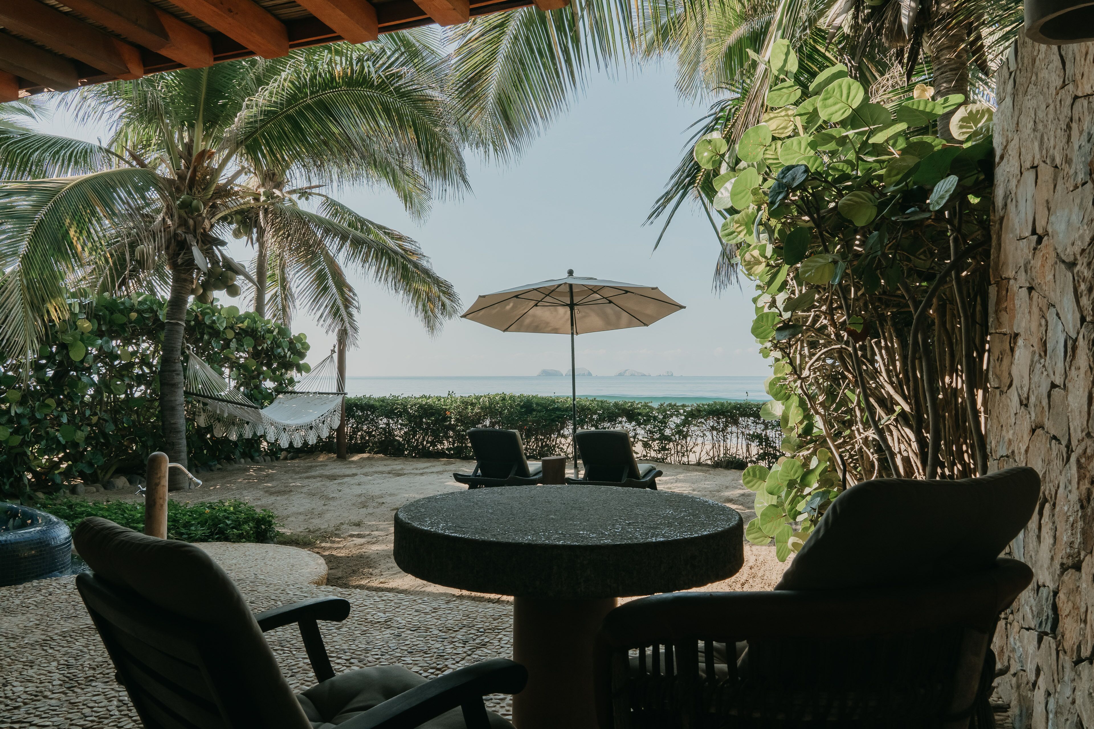 A patio with a round table and chairs, a hammock, and a view of the ocean.