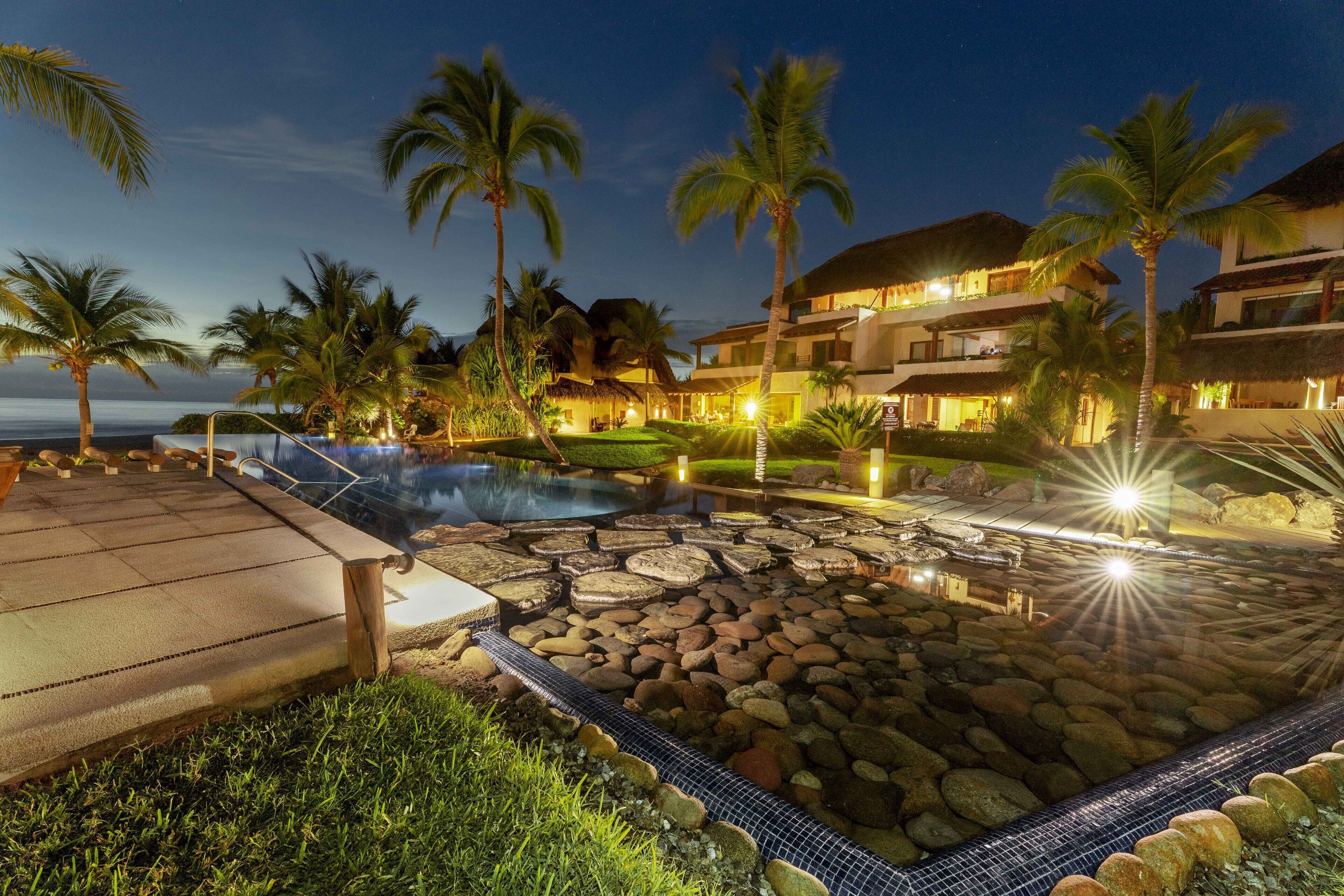 Um resort com piscina, palmeiras e vista para o oceano.